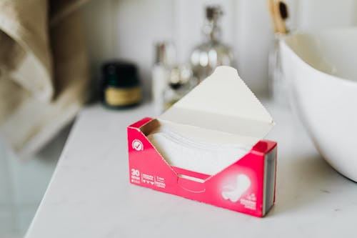 Free From above of open package of sanitary napkins placed on white surface near ceramic sink in modern bathroom Stock Photo