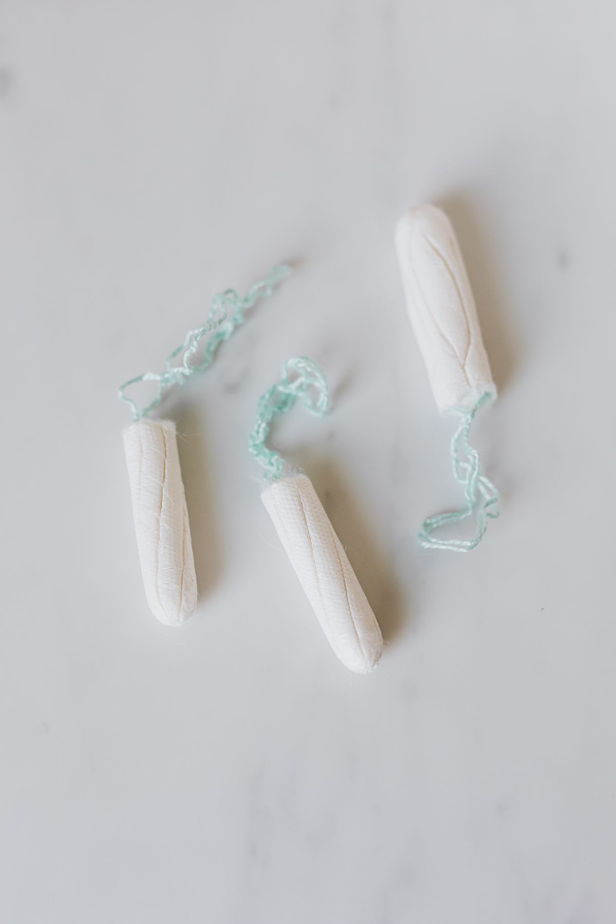 Three cotton tampons with pale green strings arranged on a white marble surface
