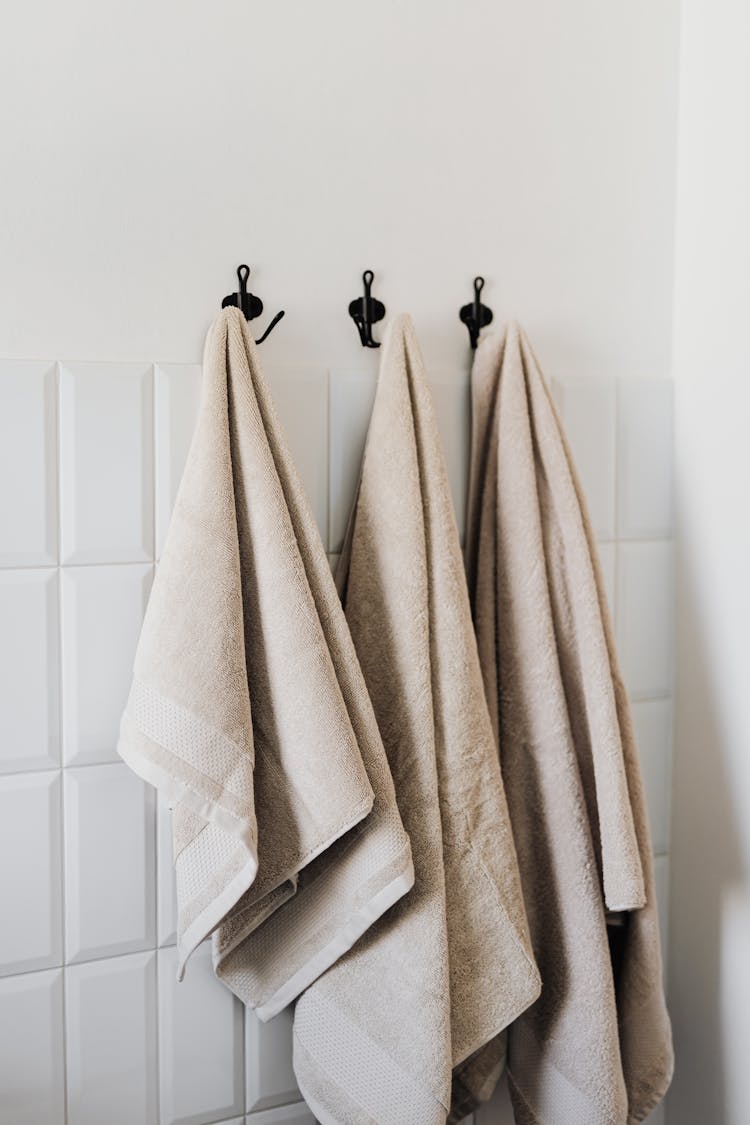 Set Of Beige Towels On Hooks In Bathroom