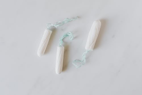 Top view of three hygienic cotton tampons placed on white marble patterned surface