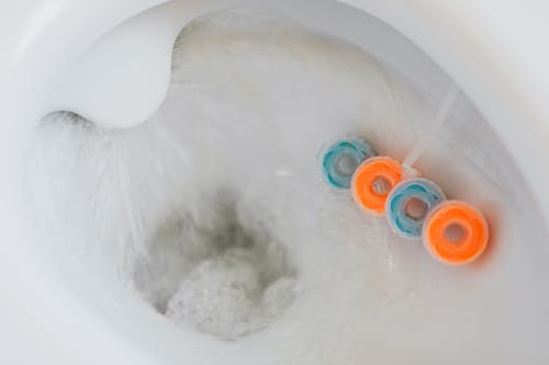 From above of flushing water in toilet bowl with cleaner and freshener block