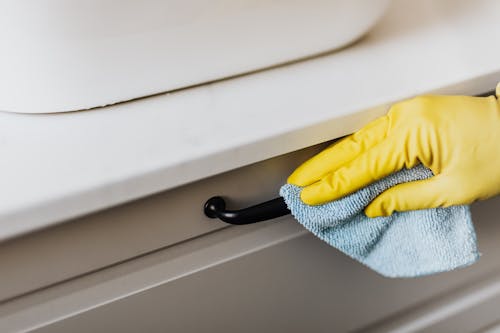Free From above of crop faceless person in yellow gloves cleaning handle of cabinet with microfiber cloth in modern bright bathroom Stock Photo