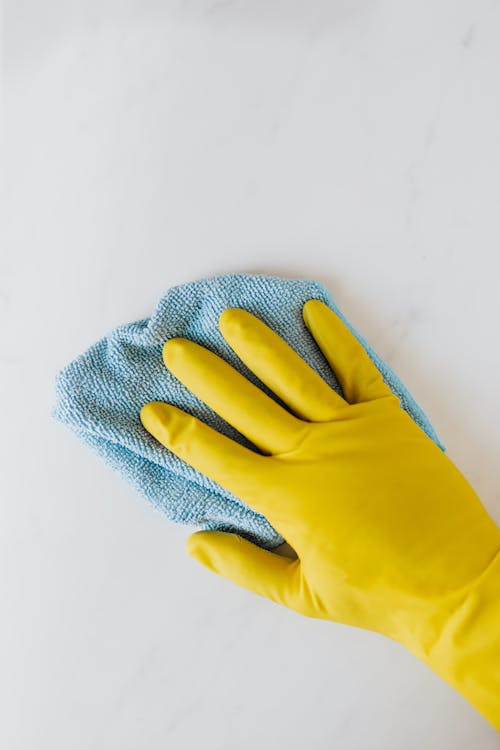 Free Crop unrecognizable person in yellow gloves cleaning white surface Stock Photo