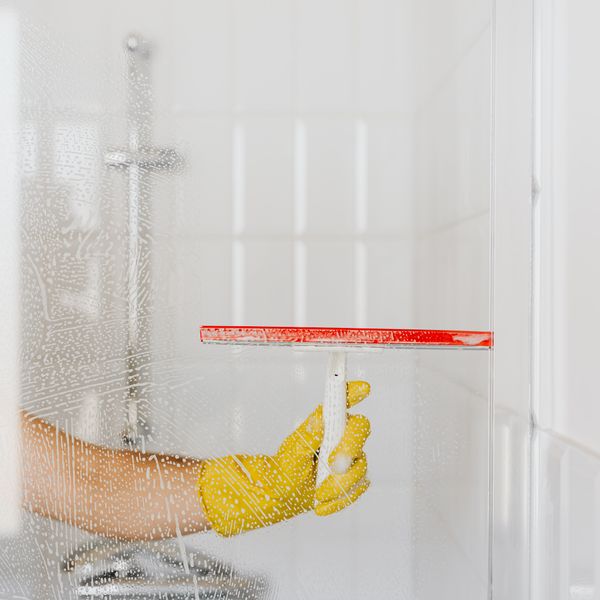 Cleaner squeegeeing a glass shower door until the panel is spotless