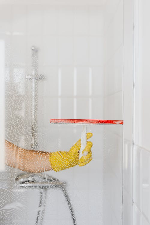 Crop person cleaning glass shower unit as part of their spring cleaning routine