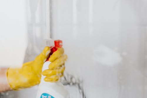 Free Person in glove spraying detergent at walk in shower glass Stock Photo