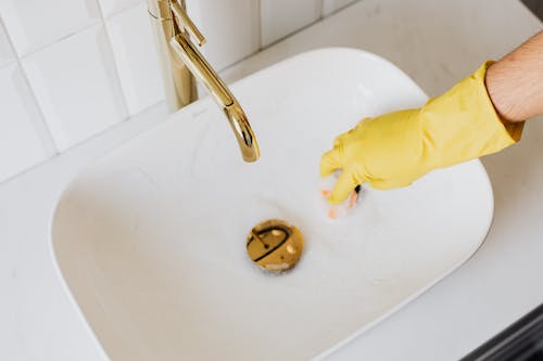 Person in glove using sponge with detergent for cleaning sink