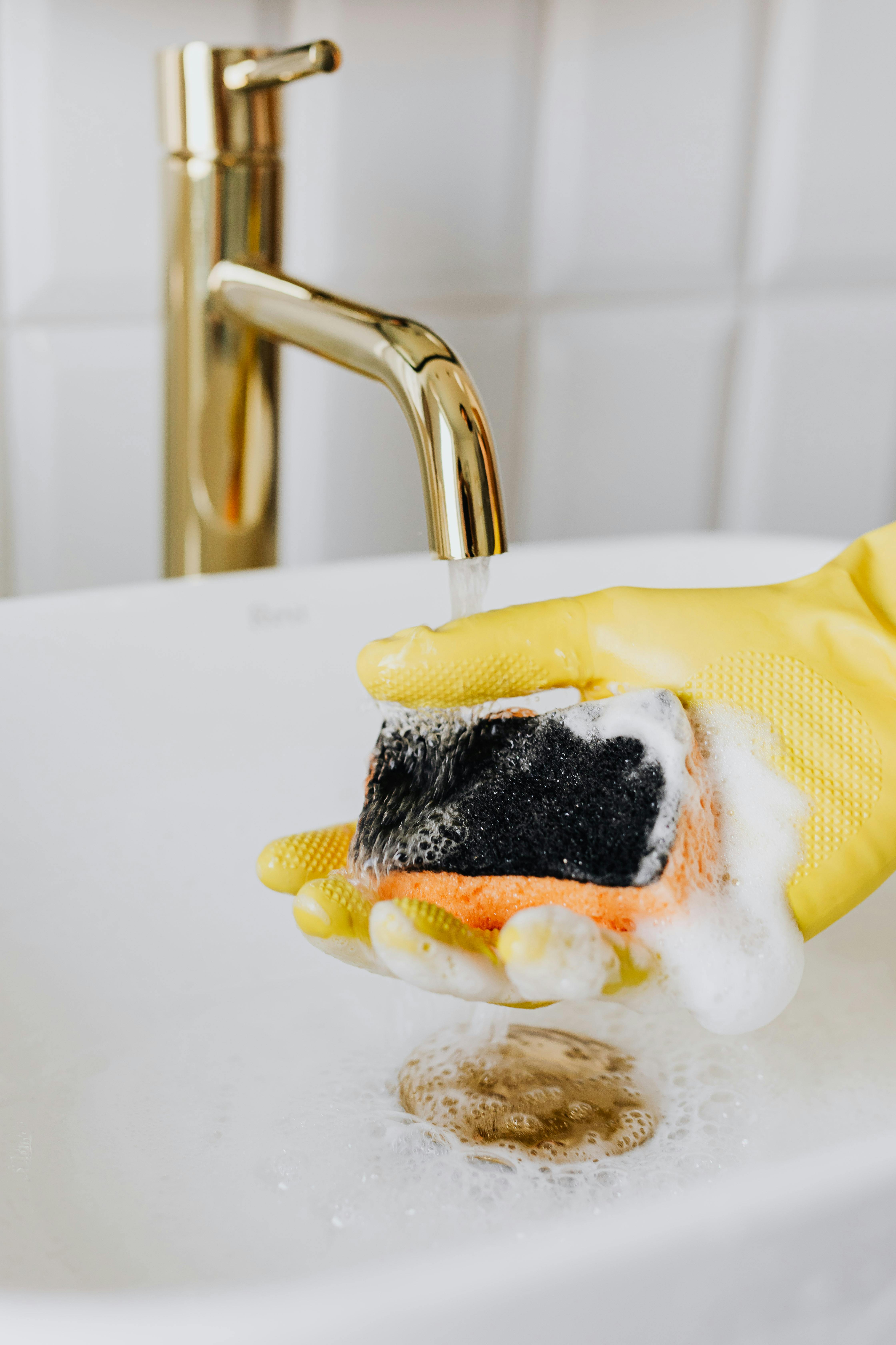 person in glove rinsing sponge with cleaning agent under running water