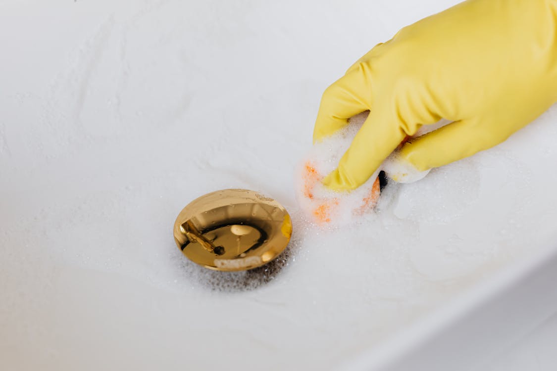 Person in glove using sponge and detergent for washing bathroom sink