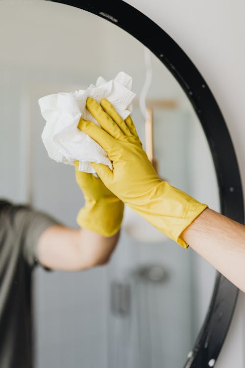 Crop man cleaning mirror in bathroom