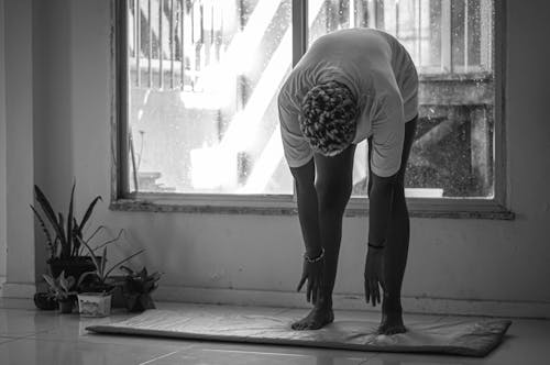 Free Grayscale Photo of a Person Stretching Near a Glass Window Stock Photo