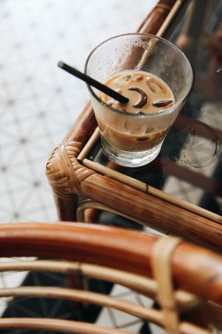 Elevated view of iced coffee in a glass with straw on wicker table for a refreshing break.