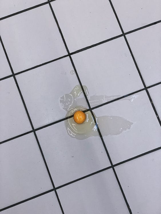 Broken egg without shell on tiled floor