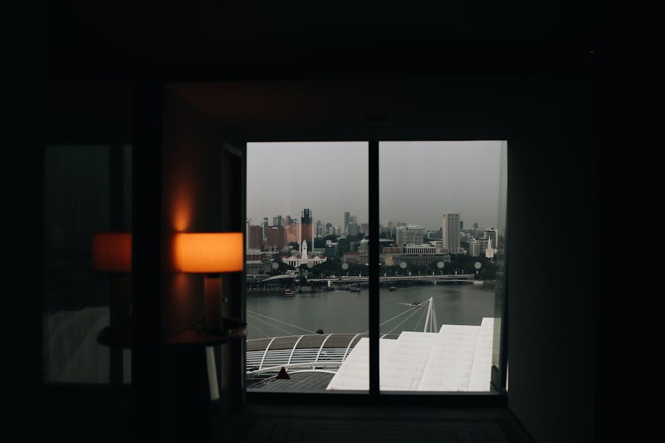 A dimly lit room with a cityscape view through the window on an overcast day.