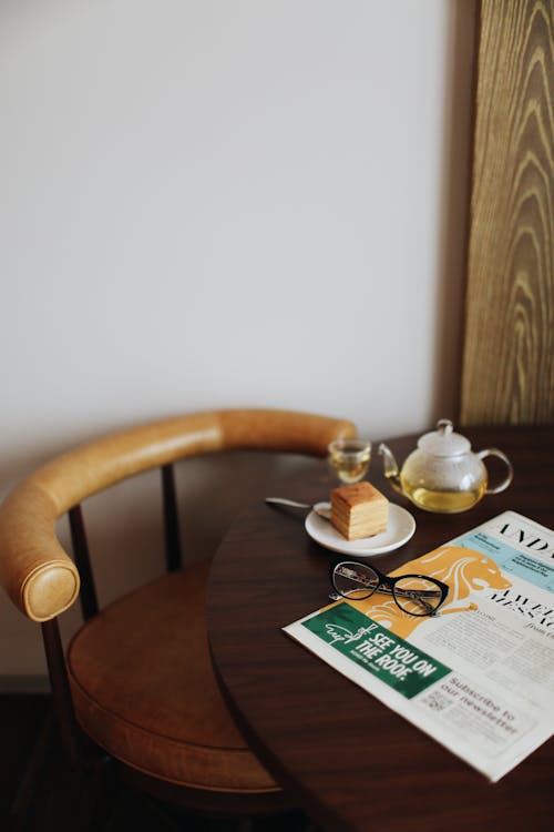Free Chair against table served with newspaper eyeglasses and tea pot Stock Photo