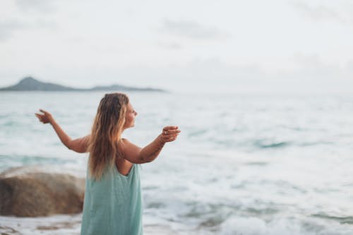 Relaxed young lady admiring waving sea with raised arms