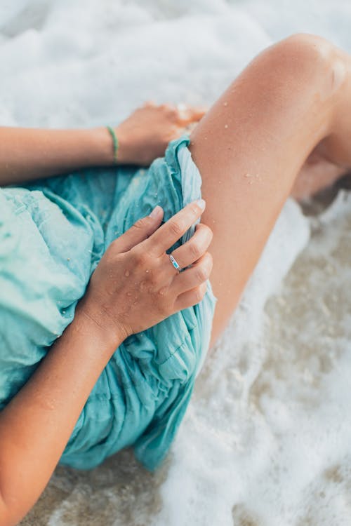 Crop woman relaxing on wet foamy sandy beach