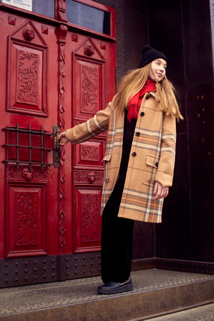 Photo Of A Woman In A Beige Coat Opening A Red Door