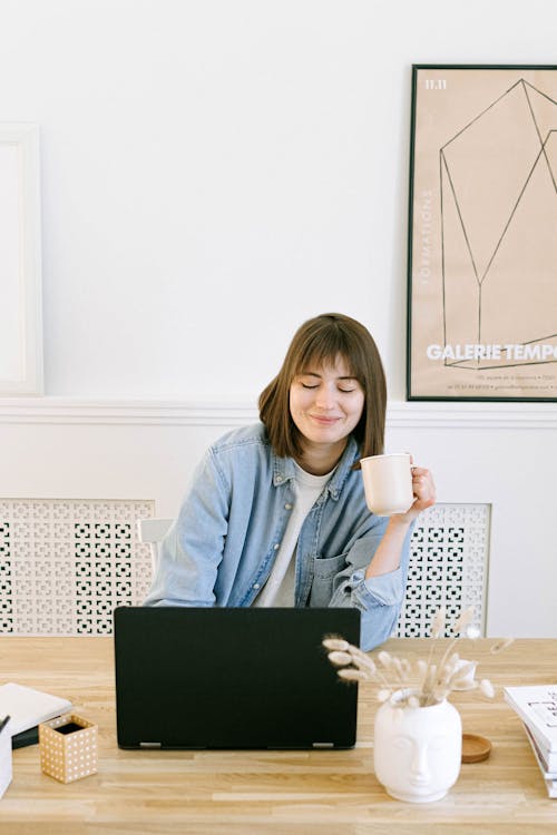 Free Woman Drinking Coffee and Looking at a Laptop Stock Photo