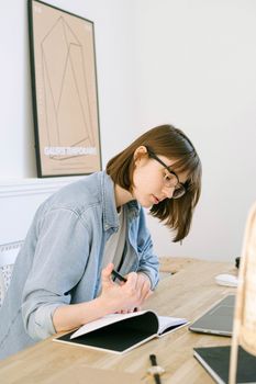 一位专注的年轻女性在家庭办公桌上，借着自然阳光写笔记