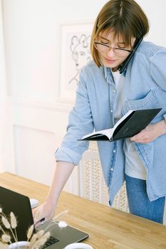 年轻女子在家庭办公桌上工作时，同时操作着笔记本和手机