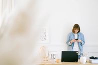 一位穿着休闲牛仔装的女性在明亮、极简风格的家庭办公室里用智能手机发短信