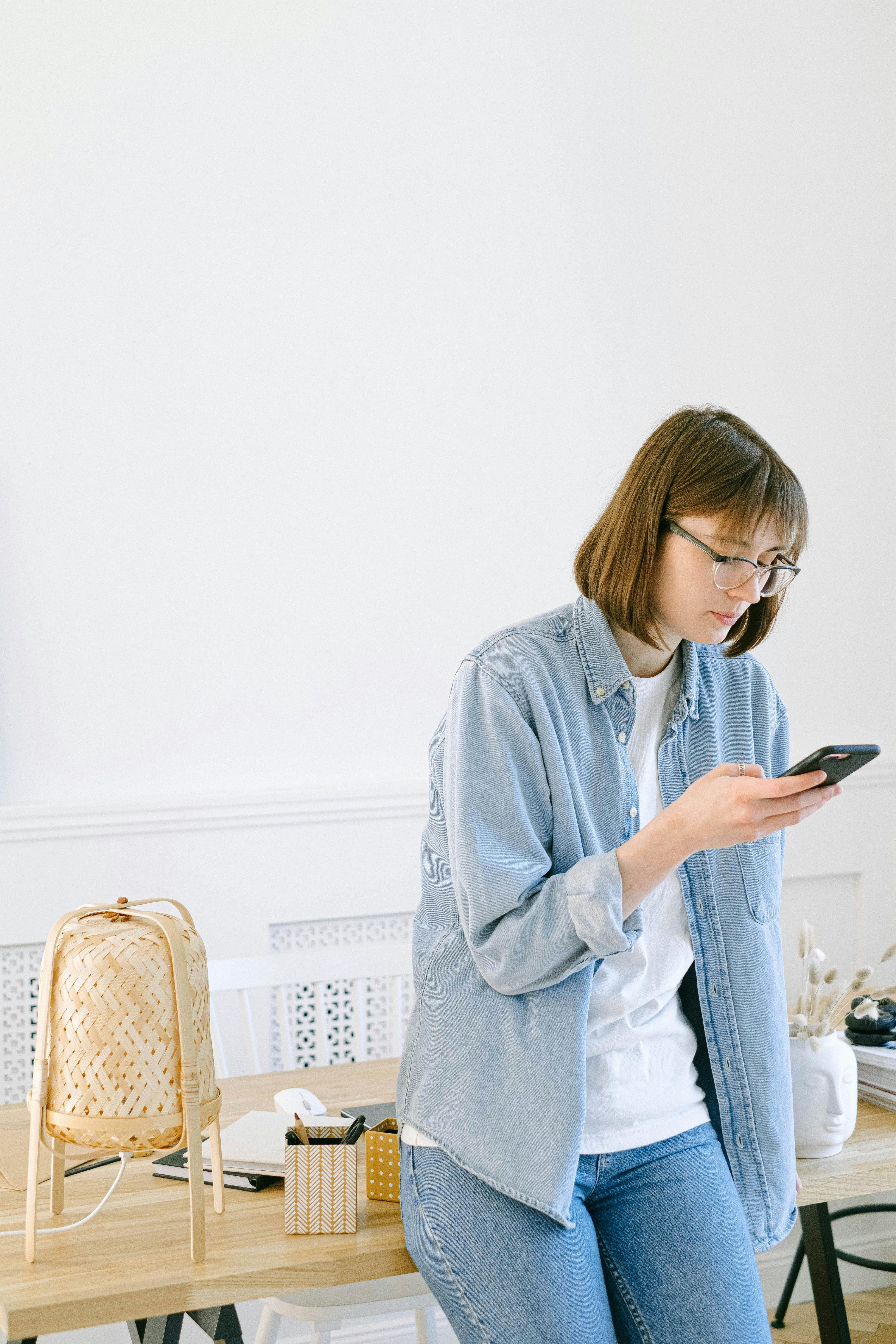 A woman in casual wear using her smartphone in a tranquil home office environment.