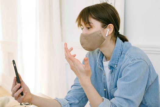 一名女子戴着口罩，在室内用智能手机进行视频通话