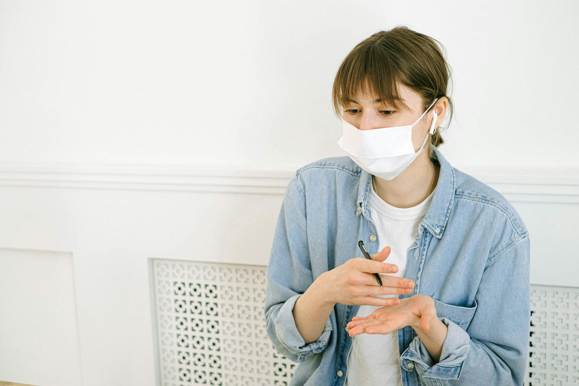 Woman applying hand sanitizer while wearing a mask indoors, practicing hygiene.