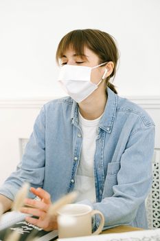 一位穿着牛仔夹克、戴着口罩的女人正在家庭办公室的办公桌前工作