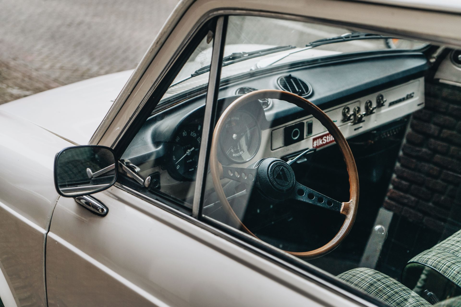 Close-up shot of a vintage car interior featuring a wooden steering wheel and retro dashboard design.