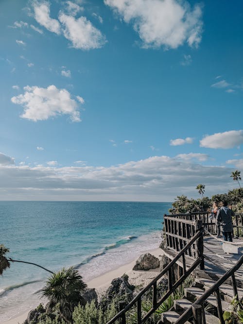 People Standing on Wooden Dock Near Sea Under Blue and White Cloudy Sky