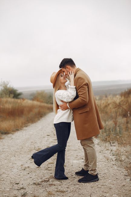 Full body of romantic young couple in trendy outfits embracing each other while standing on pathway in countryside against cloudy sky