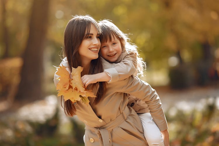 Happy Mother Giving Daughter Piggyback Ride In Park