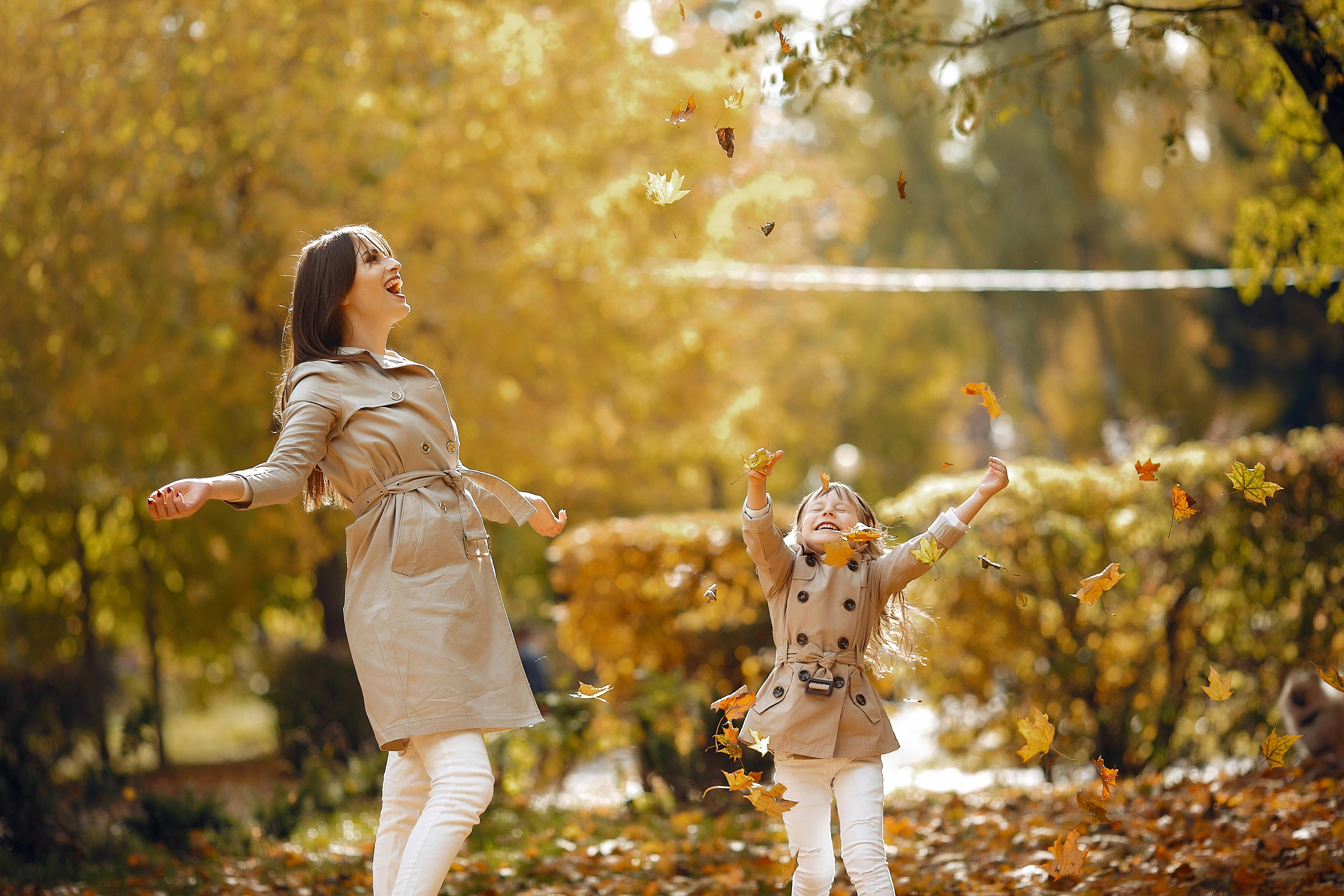 excited mother and daughter throwing maple leaves in air