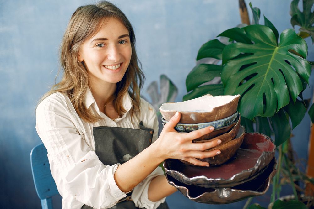 Ceramicist in an apron holding a stack of hand-built bowls in her studio — photo by Gustavo Fring on Pexels