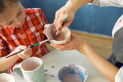 Crop artisan and little girl painting earthware in workshop