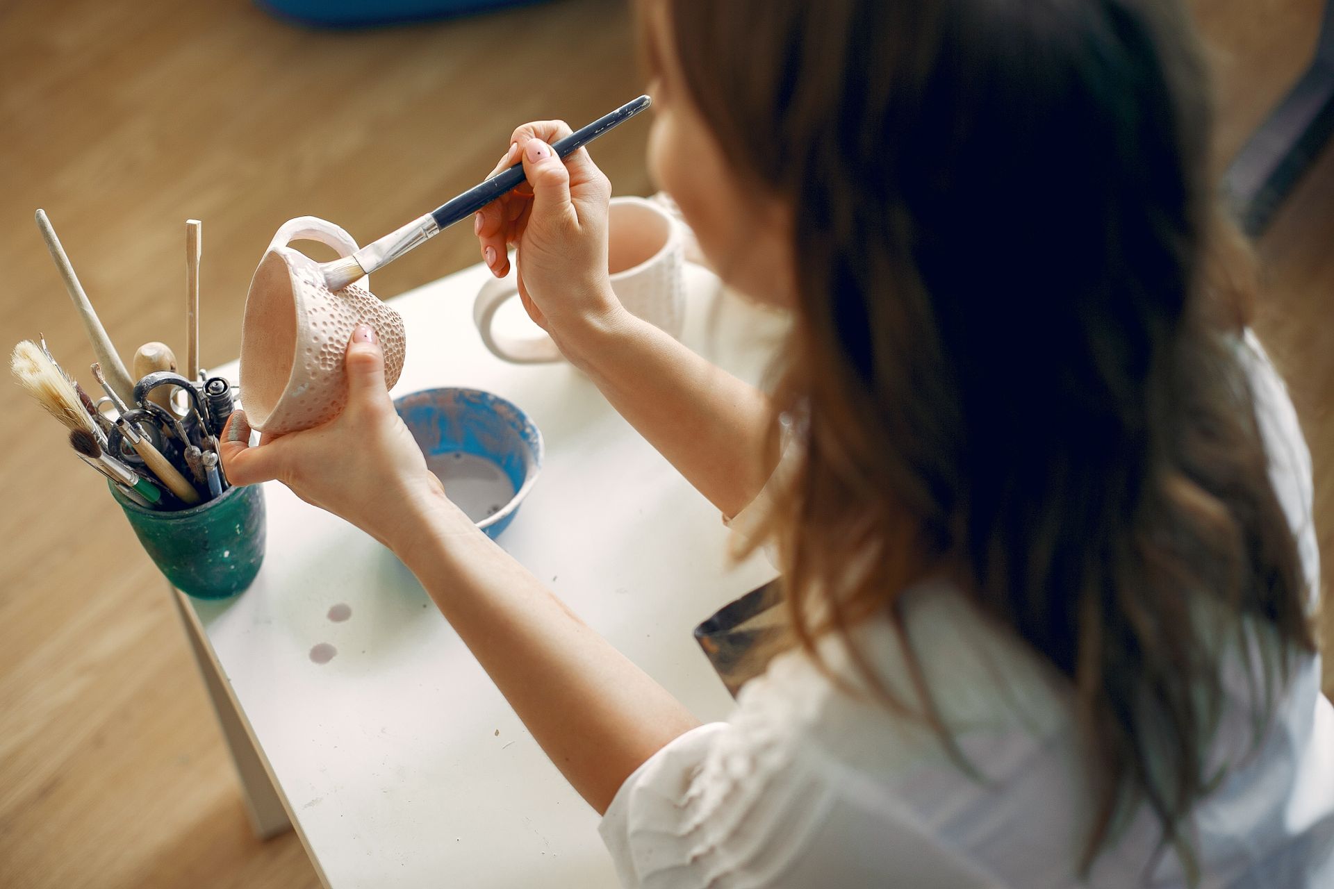 A craftswoman meticulously paints a handmade ceramic mug in her artistic workshop.