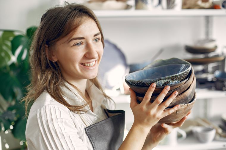 Ceramist holding a stack of handmade bowls in a sunlit workshop — photo by Gustavo Fring on Pexels