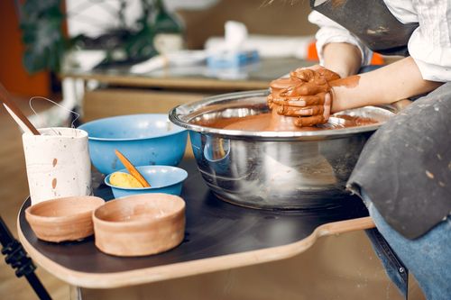 Free Crop anonymous female ceramist in black apron sitting against pottery wheel and molding clay pot while working in creative pottery studio Stock Photo