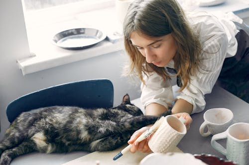 Free Woman Painting Mugs with Lying Cat Stock Photo