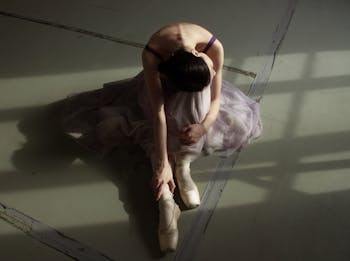 Unrecognizable graceful ballet dancer resting on floor