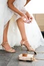 Crop unrecognizable bride in white dress and high heeled shoes holding lipstick in hands while preparing for wedding ceremony