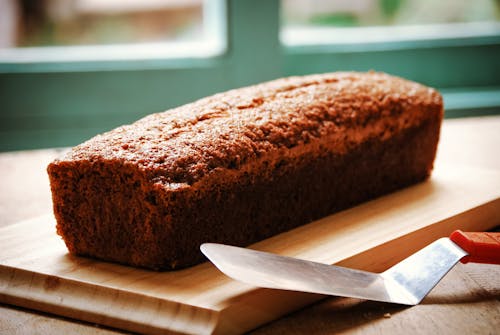 High angle of whole crispy fresh baked banana bread served on wooden cutting board and placed on table with spatula