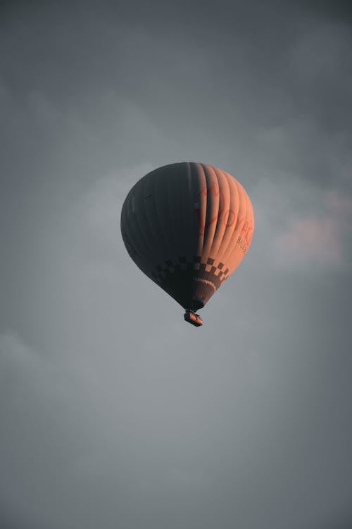 From below of big air balloon flying in gray cloudy sky during sunset