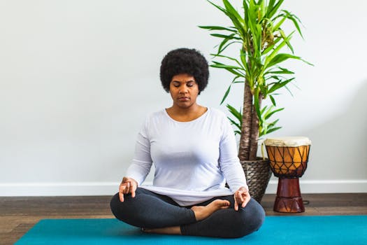 African American woman meditating indoors on a yoga mat with a plant and drum nearby.