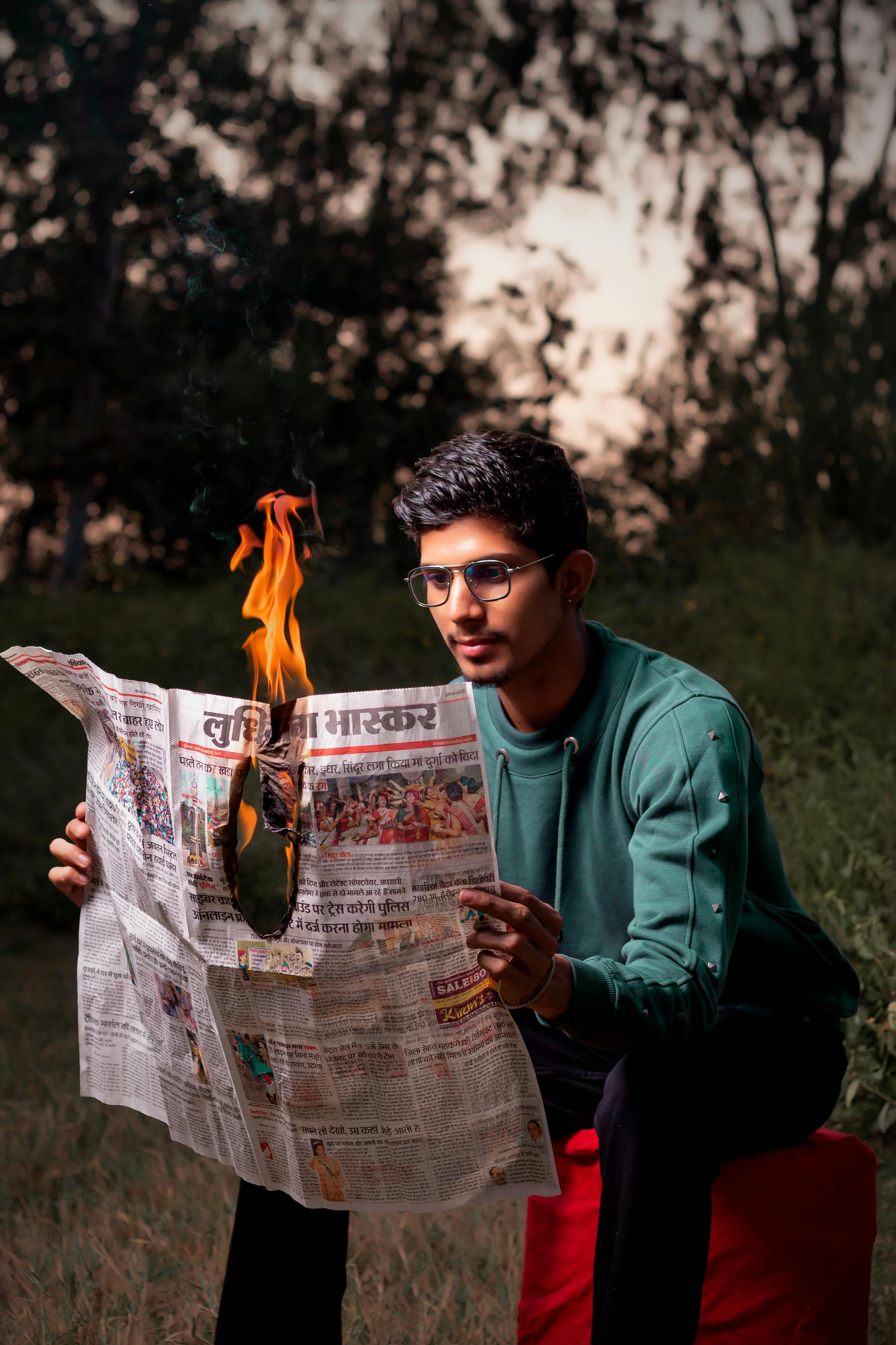 man in long sleeves holding a burning newspaper