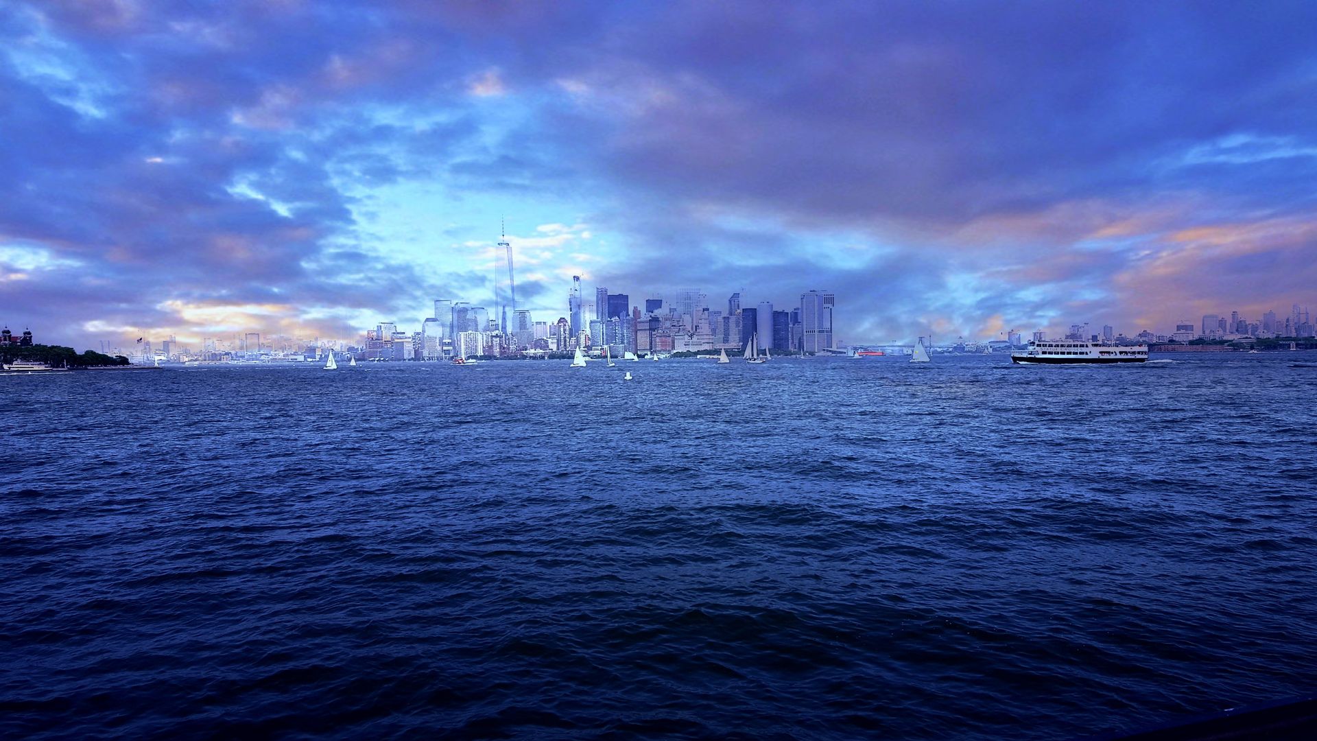 Beautiful view of New York City skyline from the water at dusk with sailboats and a ferry.