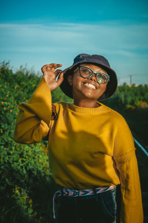 Free Cheerful woman in glasses and bucket hat smiling in a sunny outdoor setting. Stock Photo