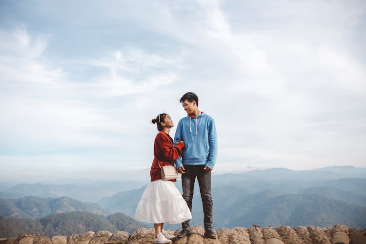 A Sweet Couple Standing On The Edge Of A Cliff While Looking At Each Other